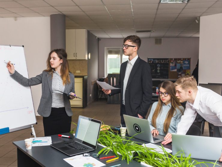 employee productivity a person standing in front of a whiteboard with a person and a person standing in front of a table with laptops and papers